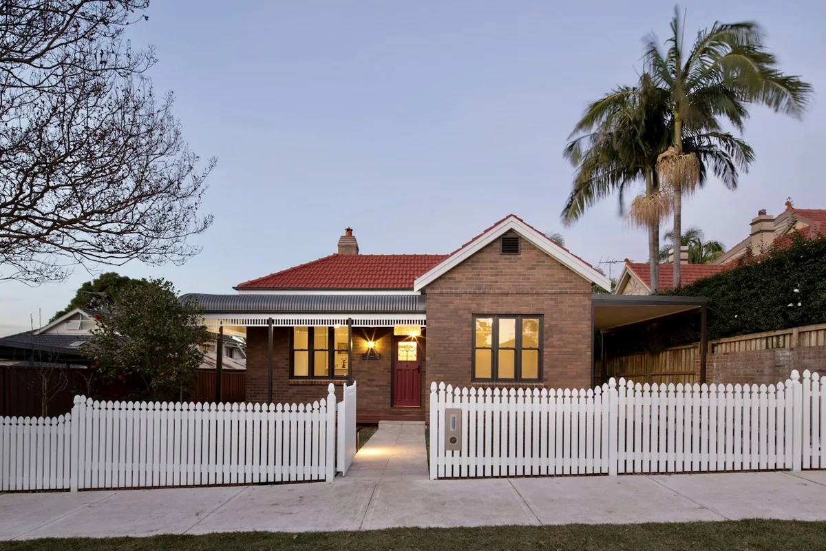 A warmly lit family home behind a white picket fence